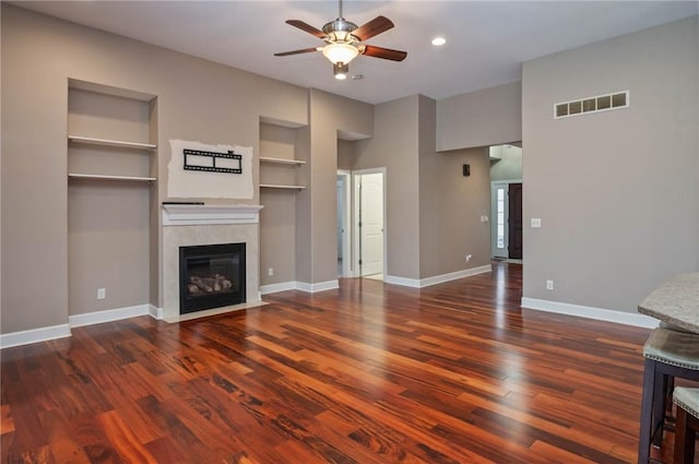 unfurnished living room featuring built in features, wood finished floors, visible vents, baseboards, and a fireplace