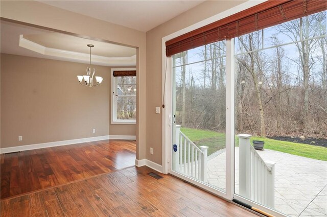 entryway with visible vents, baseboards, a chandelier, a tray ceiling, and wood finished floors