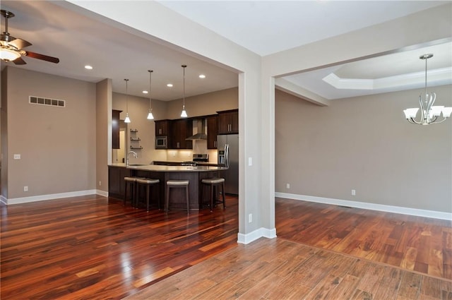 kitchen with a breakfast bar, open floor plan, stainless steel appliances, wall chimney range hood, and dark brown cabinets