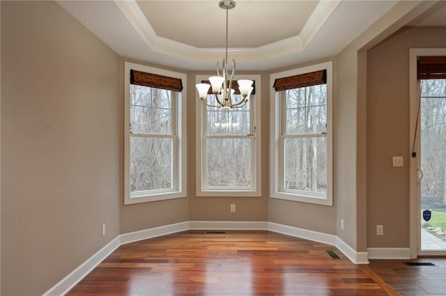 unfurnished dining area with visible vents, baseboards, an inviting chandelier, dark wood-style flooring, and a raised ceiling