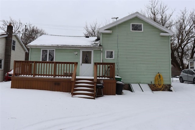 snow covered back of property with a wooden deck