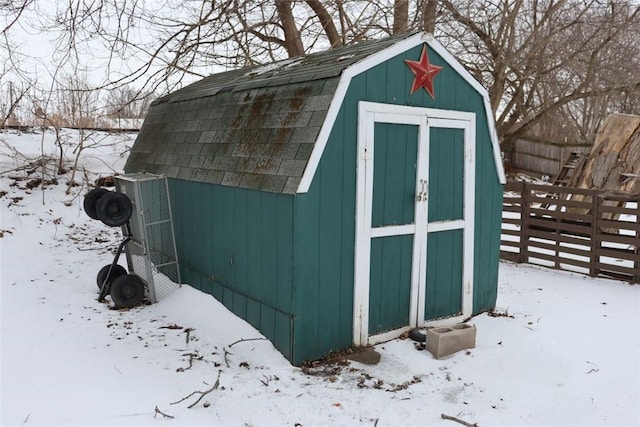 snow covered structure with a storage shed, fence, and an outbuilding