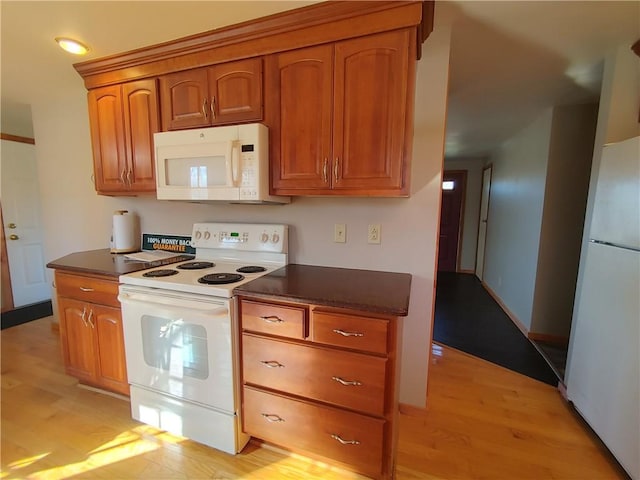 kitchen featuring light wood-type flooring, white appliances, dark countertops, and brown cabinetry