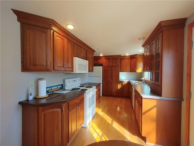 kitchen with white appliances, brown cabinetry, a sink, glass insert cabinets, and light wood-type flooring