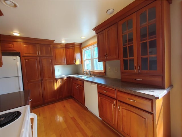 kitchen with white appliances, brown cabinetry, glass insert cabinets, and a sink