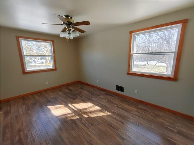 empty room with a wealth of natural light, visible vents, baseboards, and wood finished floors