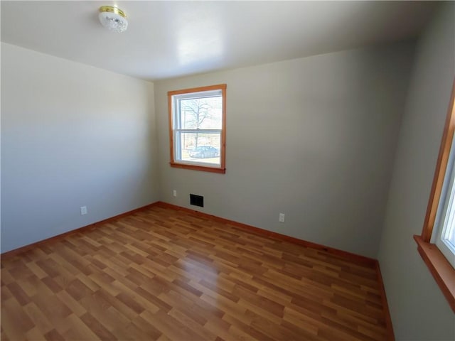 spare room featuring light wood-style floors, visible vents, and baseboards