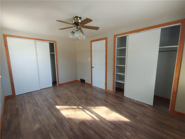 unfurnished bedroom with baseboards, two closets, wood finished floors, and a ceiling fan