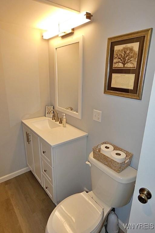 bathroom with toilet, vanity, baseboards, and wood finished floors