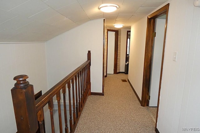 hallway with vaulted ceiling, an upstairs landing, baseboards, and light carpet