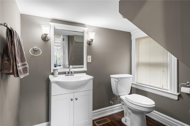 half bath featuring vanity, toilet, baseboards, and visible vents