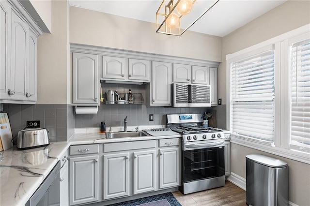 kitchen featuring stainless steel range with gas stovetop, backsplash, light stone countertops, and a sink