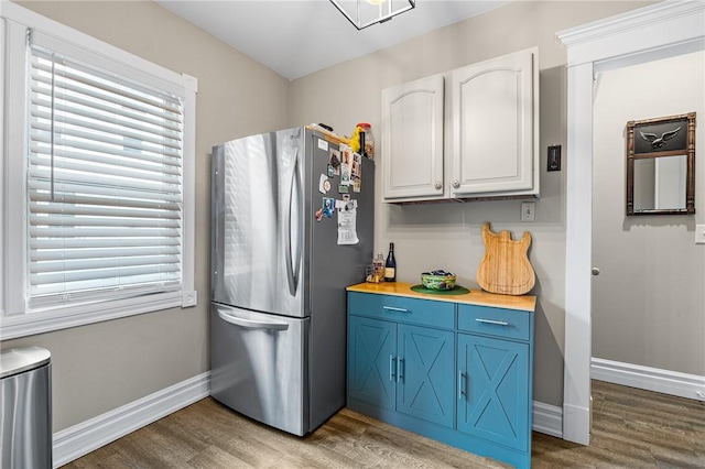 kitchen featuring blue cabinets, white cabinetry, freestanding refrigerator, light wood-style floors, and baseboards