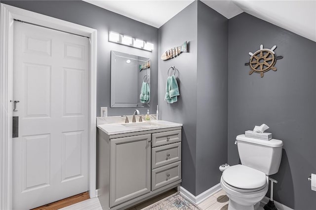 half bath featuring baseboards, toilet, vanity, and vaulted ceiling