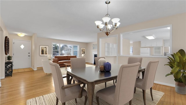 dining room with baseboards, a fireplace, light wood-type flooring, and a chandelier