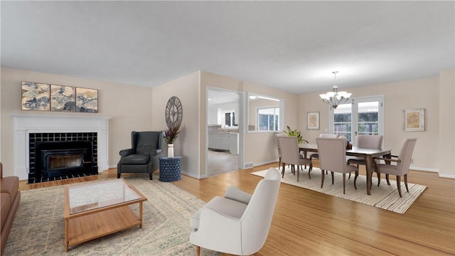 living area with baseboards, a notable chandelier, a fireplace, and light wood finished floors