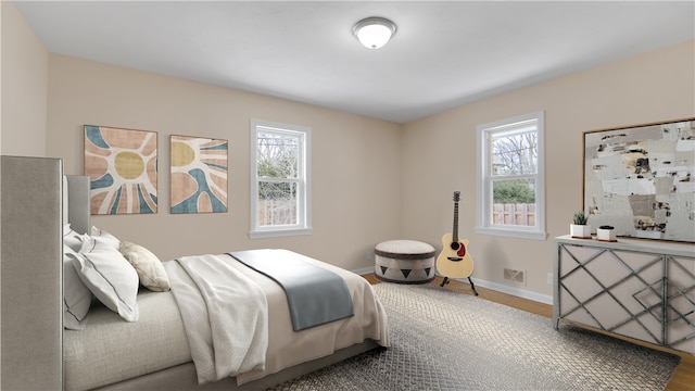 bedroom with visible vents, multiple windows, wood finished floors, and baseboards