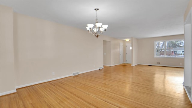 spare room with light wood-style flooring, a notable chandelier, visible vents, and baseboards