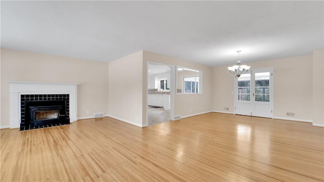 unfurnished living room featuring light wood finished floors, visible vents, baseboards, a tiled fireplace, and a notable chandelier