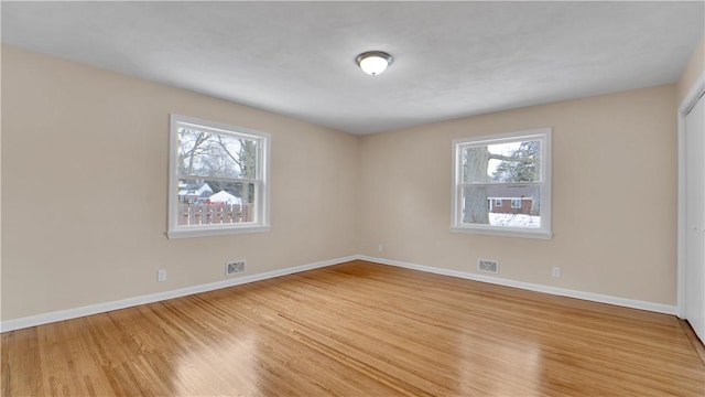 unfurnished room with wood finished floors, visible vents, and baseboards