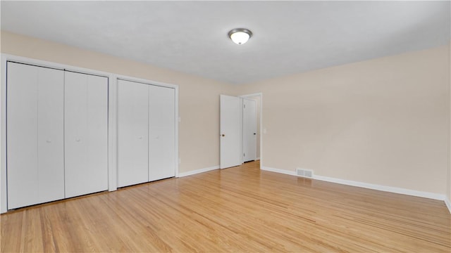 unfurnished bedroom featuring visible vents, light wood-style flooring, two closets, and baseboards