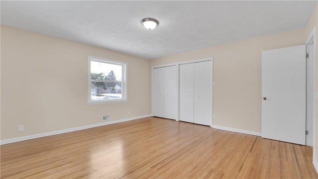 unfurnished bedroom with light wood-type flooring, baseboards, two closets, and visible vents