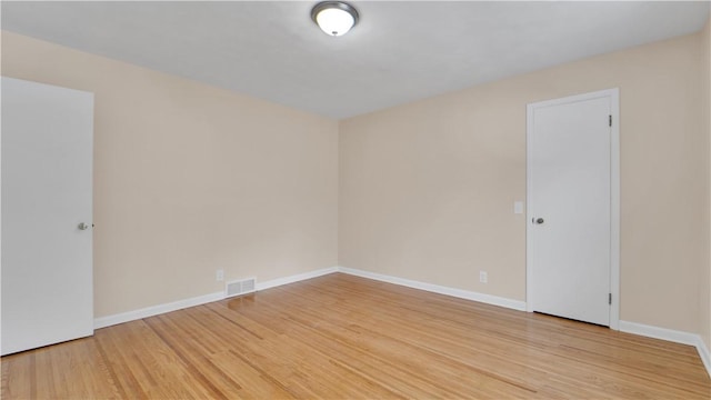 empty room with visible vents, light wood-type flooring, and baseboards