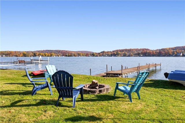 view of dock with a water view, a fire pit, and a lawn