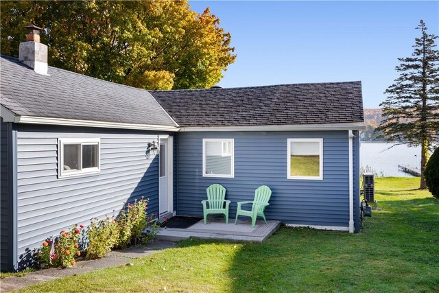 back of house with a lawn, a chimney, and a shingled roof