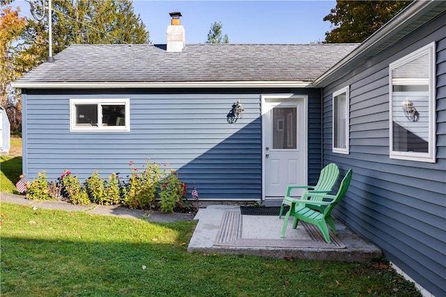 property entrance with a lawn, a chimney, and roof with shingles