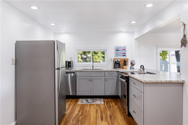 kitchen with light wood finished floors, gray cabinetry, a peninsula, stainless steel appliances, and a sink