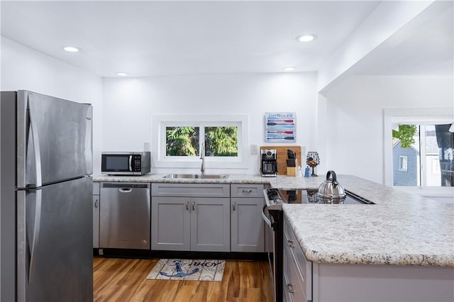 kitchen with light wood finished floors, gray cabinetry, a peninsula, stainless steel appliances, and a sink