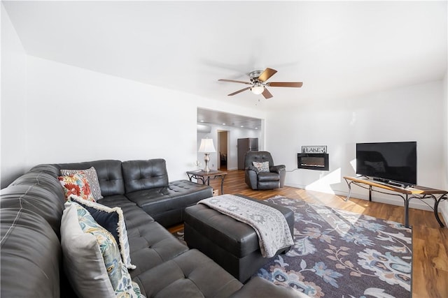 living room with a glass covered fireplace, a ceiling fan, and wood finished floors