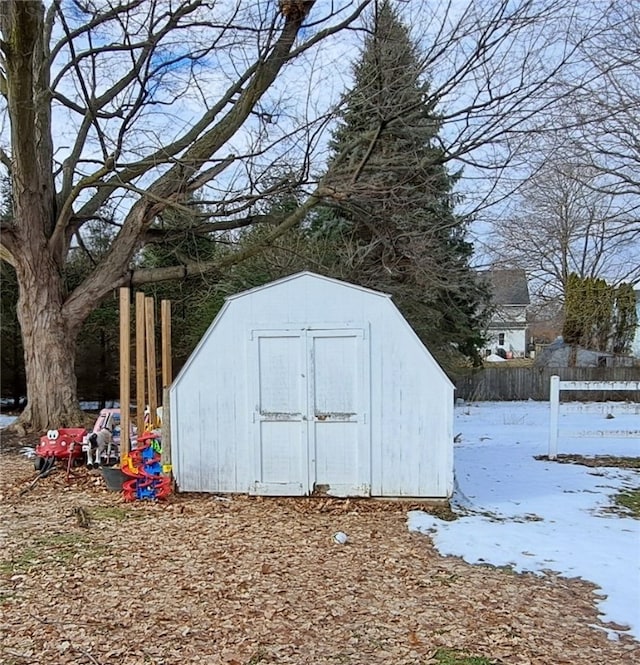 snow covered structure featuring fence, an outbuilding, and a shed