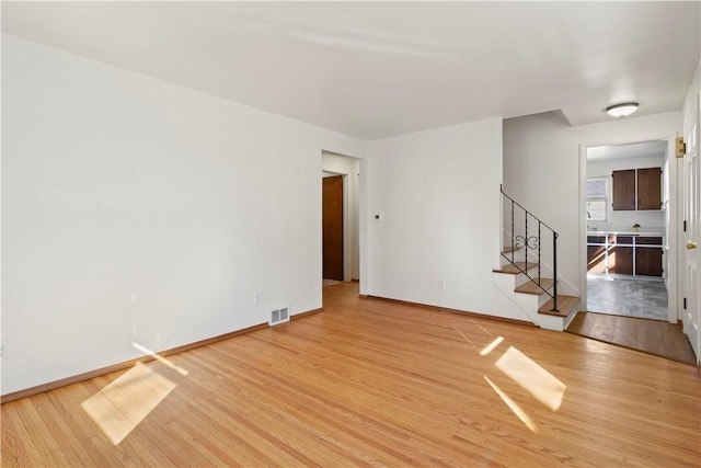 unfurnished room with visible vents, light wood-type flooring, stairs, and baseboards