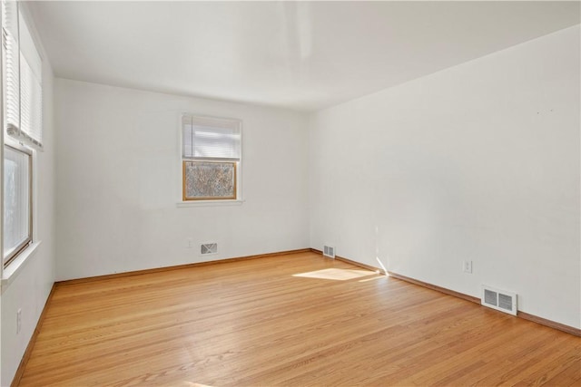 empty room with plenty of natural light, wood finished floors, and visible vents