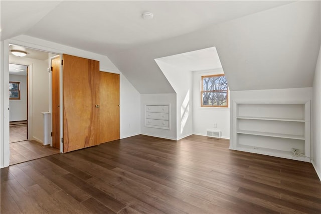 additional living space with lofted ceiling, built in shelves, wood finished floors, and visible vents