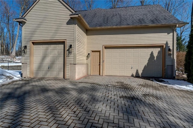 snow covered garage featuring decorative driveway