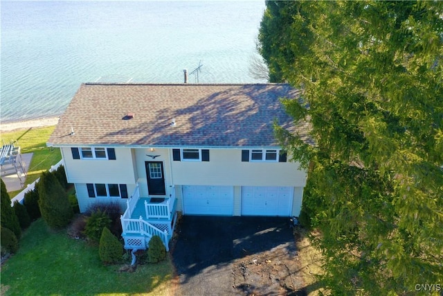 view of front of house featuring aphalt driveway, an attached garage, a water view, and a shingled roof