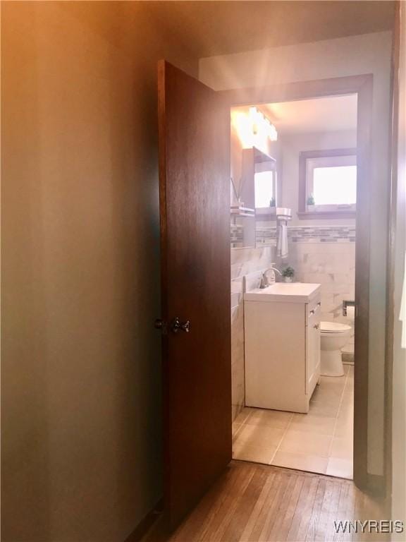 half bath featuring toilet, vanity, tile walls, and wood finished floors