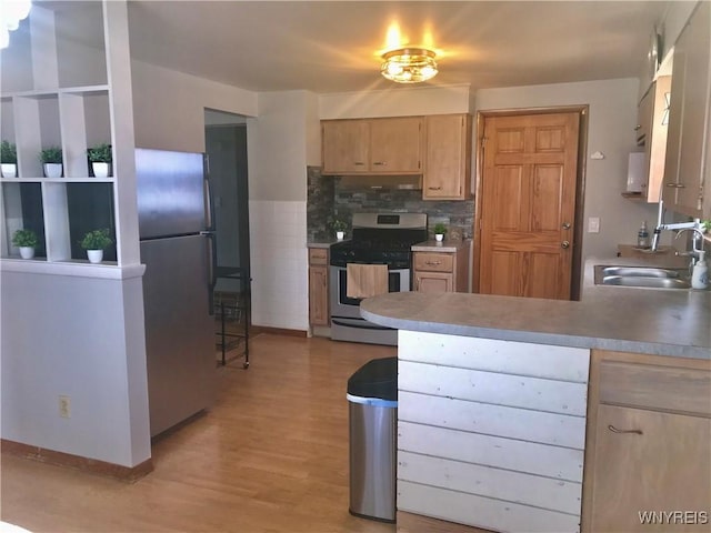 kitchen with light wood finished floors, a peninsula, a sink, light brown cabinetry, and stainless steel appliances