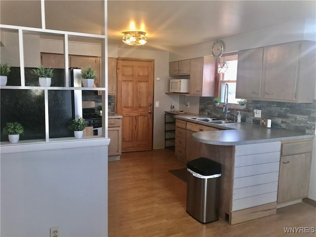 kitchen featuring a peninsula, white microwave, backsplash, and a sink