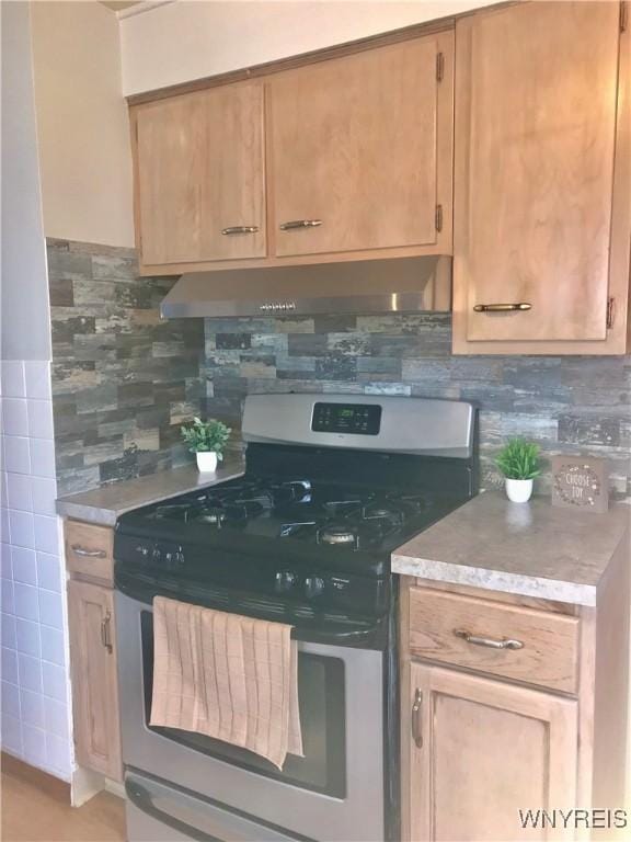 kitchen featuring gas range, light countertops, tasteful backsplash, and under cabinet range hood