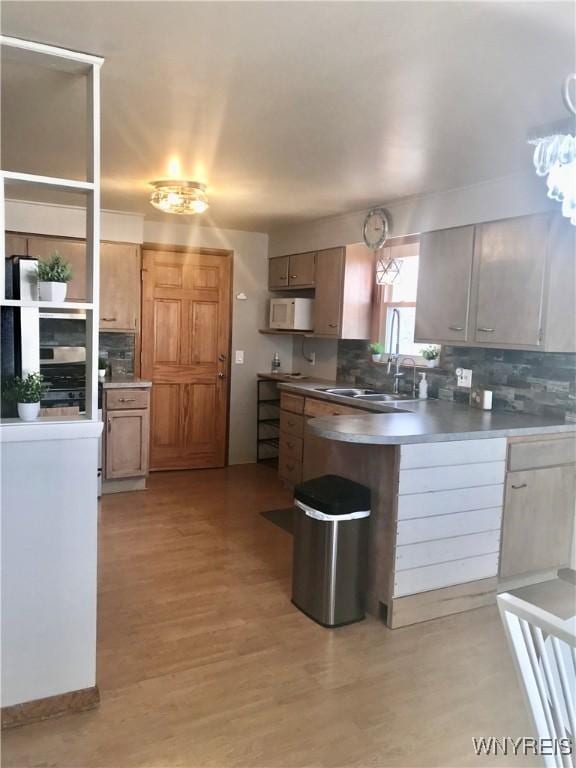 kitchen featuring a sink, decorative backsplash, white microwave, and a peninsula