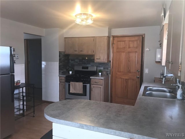 kitchen with a sink, a peninsula, freestanding refrigerator, and stainless steel gas range oven