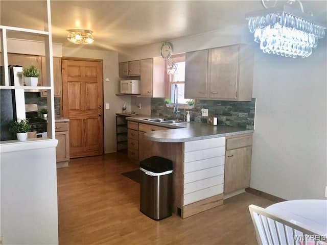 kitchen featuring white microwave, decorative backsplash, a peninsula, light wood-style floors, and a sink