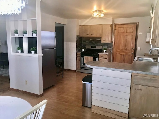 kitchen with light brown cabinetry, a sink, wood finished floors, stainless steel appliances, and a peninsula