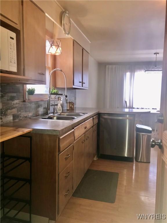 kitchen featuring tasteful backsplash, white microwave, dishwasher, and a sink