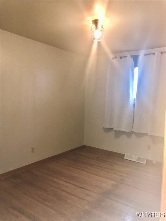 empty room with wood finished floors, visible vents, and baseboards