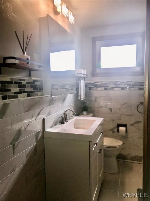 bathroom with tile patterned flooring, toilet, vanity, and tile walls